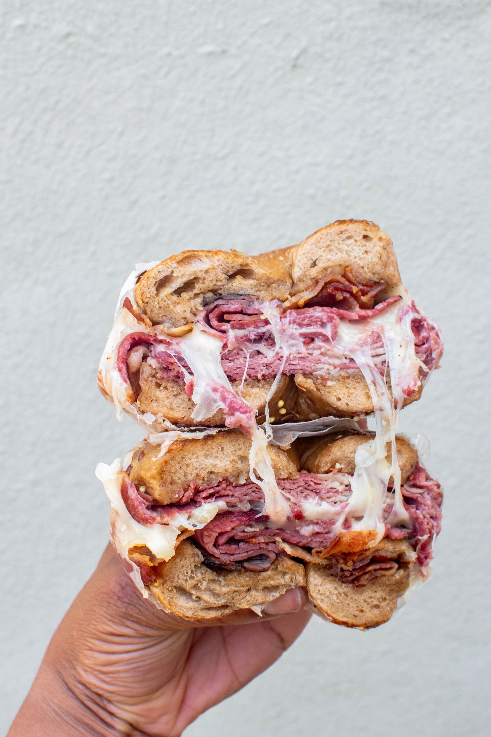 A tall pastrami sandwich with melted cheese, sliced to show the layers